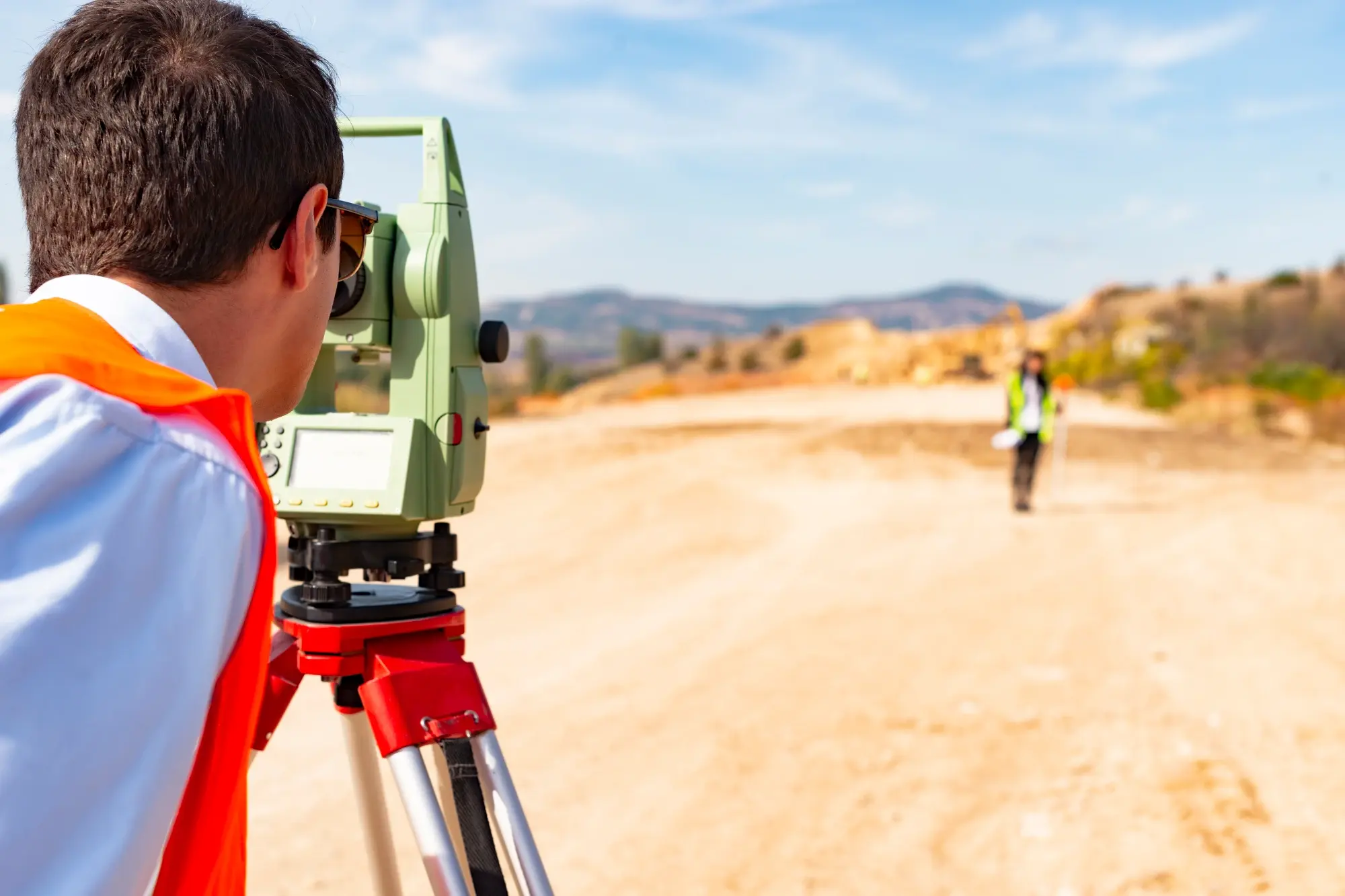 Land surveyor operating a total station with a field crew member holding a prism pole in West Texas