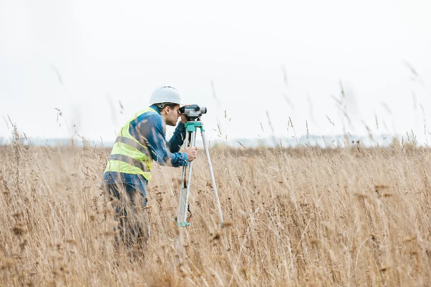 Land surveyor using a leveling instrument to establish property boundary lines in an open field