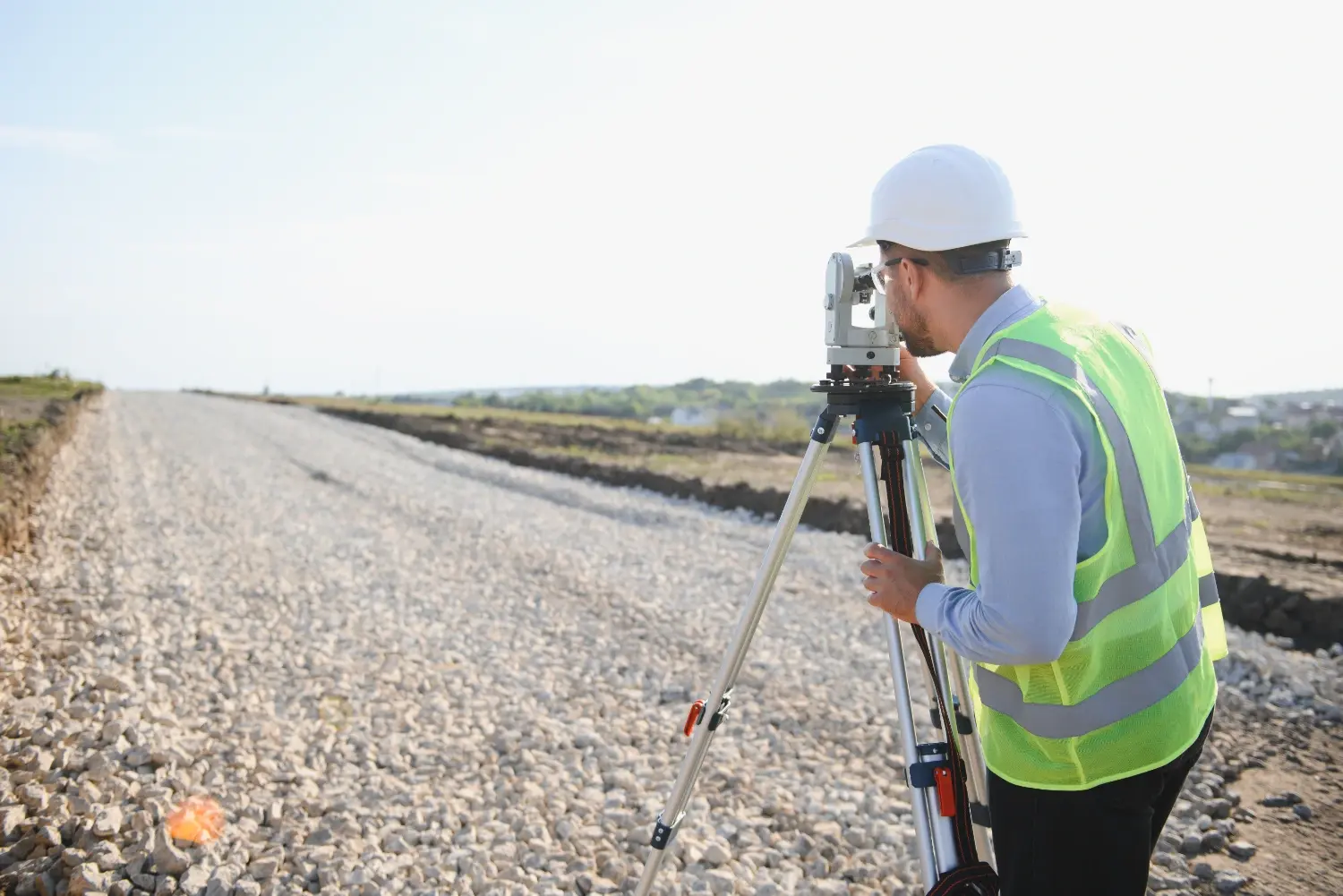 Surveyor using optical leveling equipment to verify elevation during a topographic survey of a road grading project